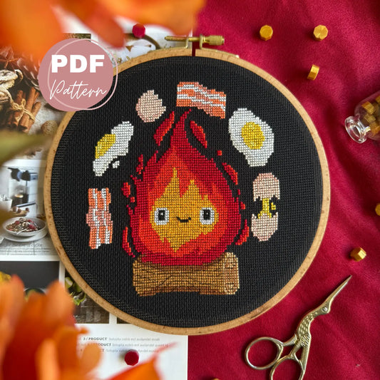 Cross-stitched design of a flame  calcifer character studio ghibli with food items on a red fabric background.